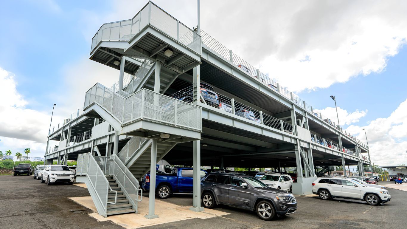 Multi-level parking garage in Puerto Rico with cars parked on multiple levels, accessible by stairs. Cloudy sky.