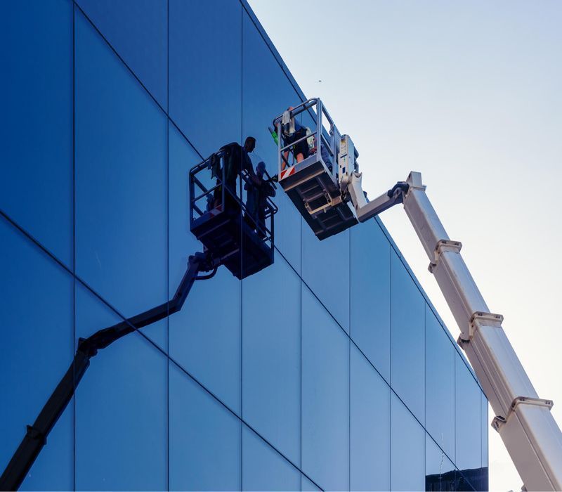 DEV Builders workers glazing on a building's exterior. They are wearing a safety vest against a blue sky.