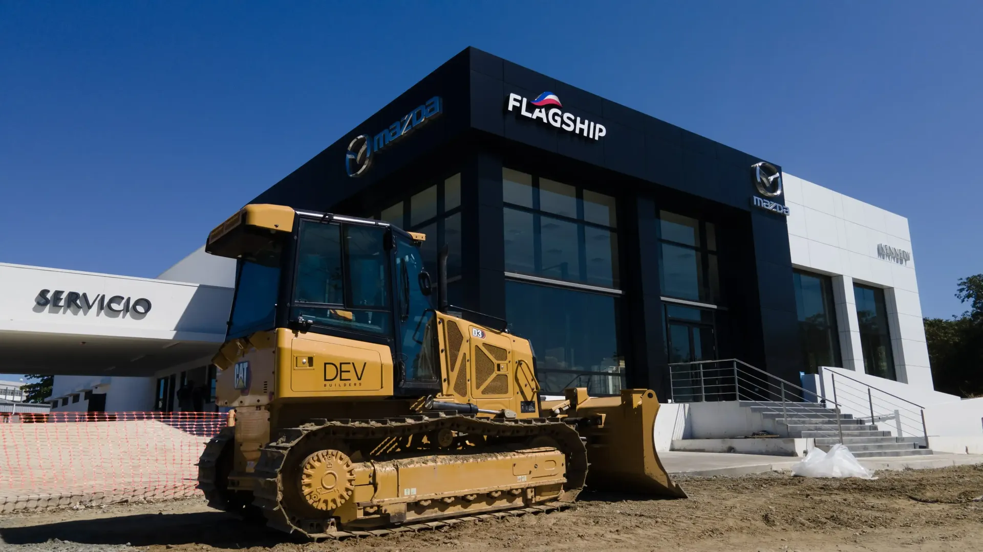A bulldozer is parked in front of a Flagship dealership built by DEV Builders Group.