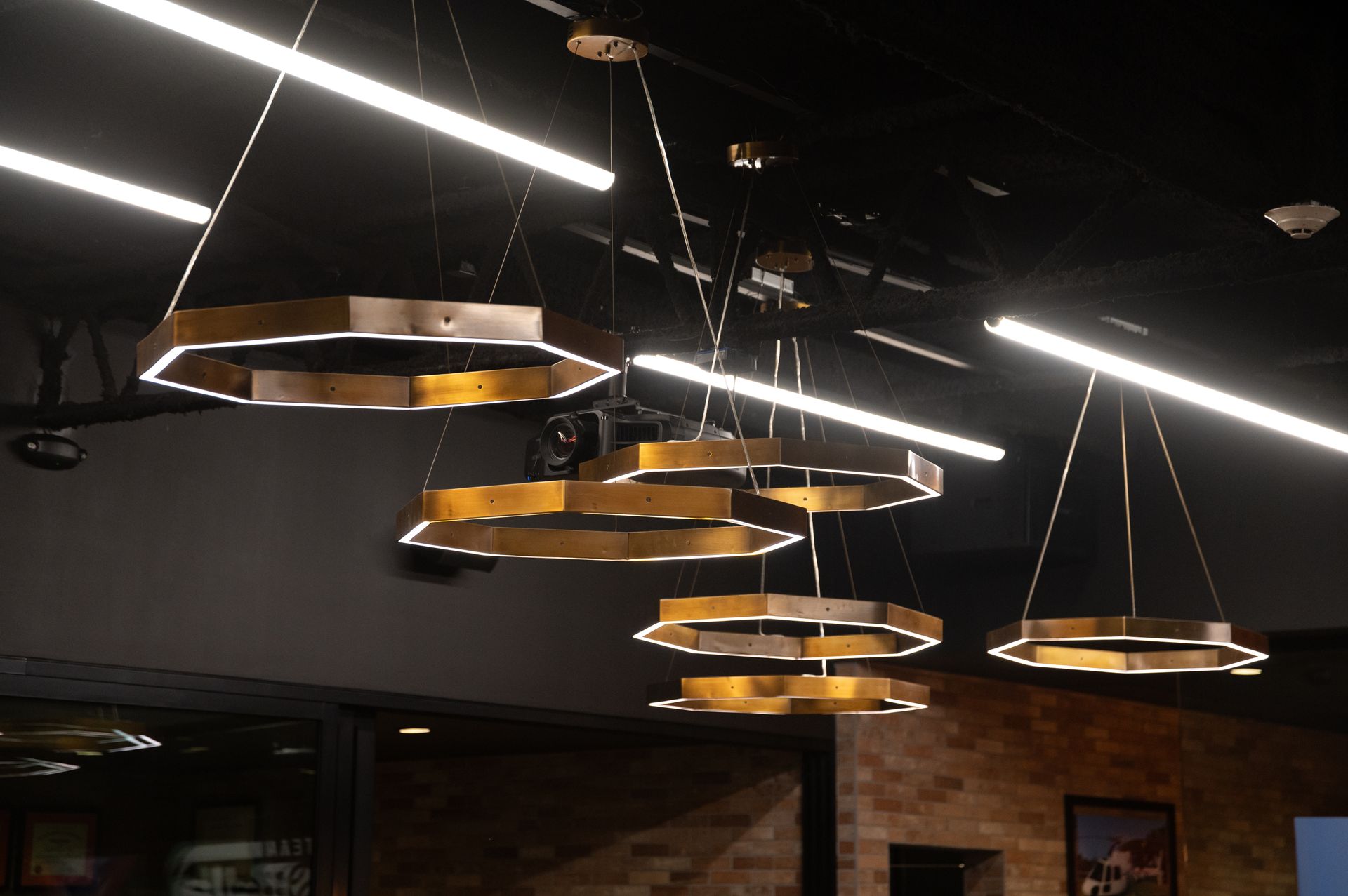 Modern pendant lights in a room with a dark ceiling, featuring hexagonal gold rings and linear fluorescent lights designed and built by DEV Builders Group.