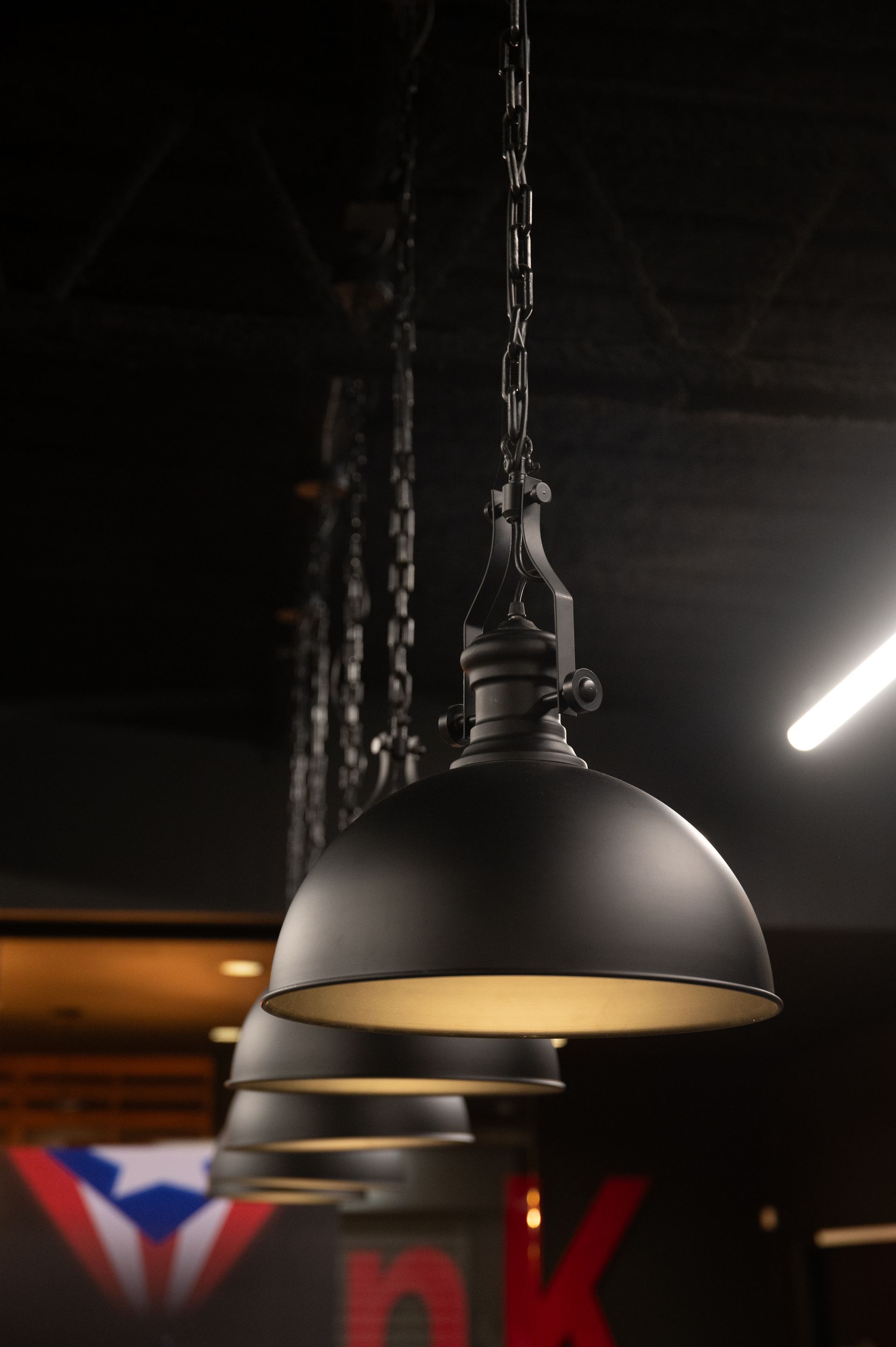 Black pendant lights hanging from the ceiling in a dark room, with a glimpse of the Puerto Rican flag in the background designed and built by DEV Builders Group.