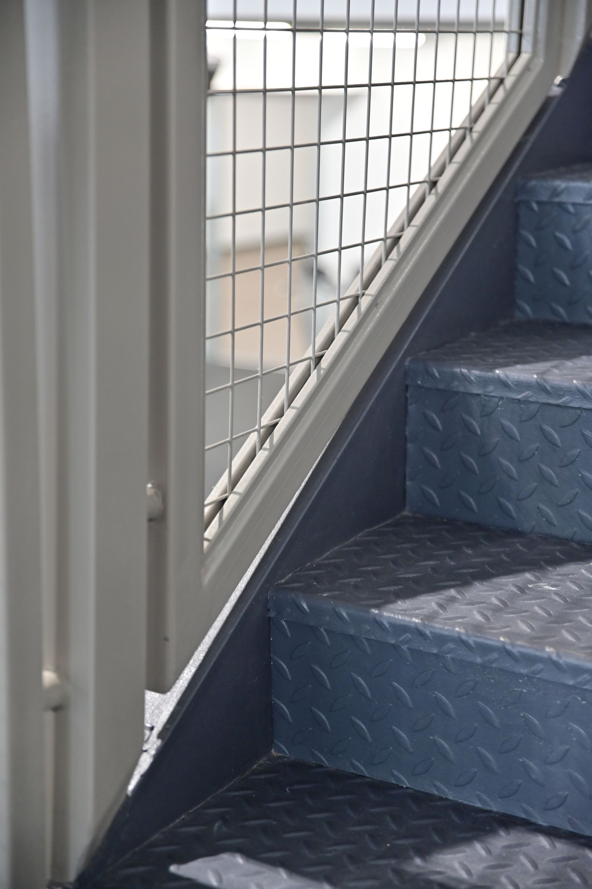 Metal staircase with diamond plate steps, grey railing, and wire mesh guard.