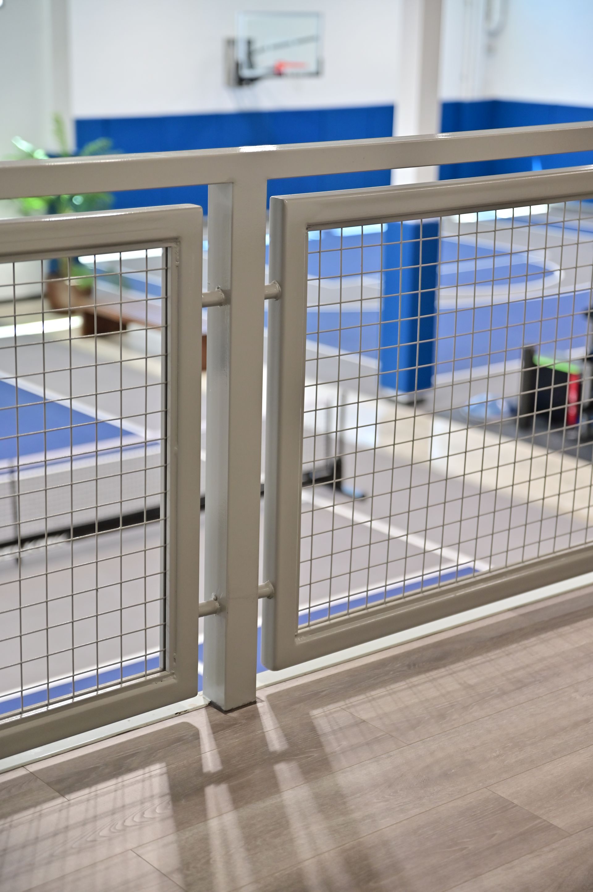 White railing with wire mesh, overlooking a blue and white floor, possibly a gym or sports area.