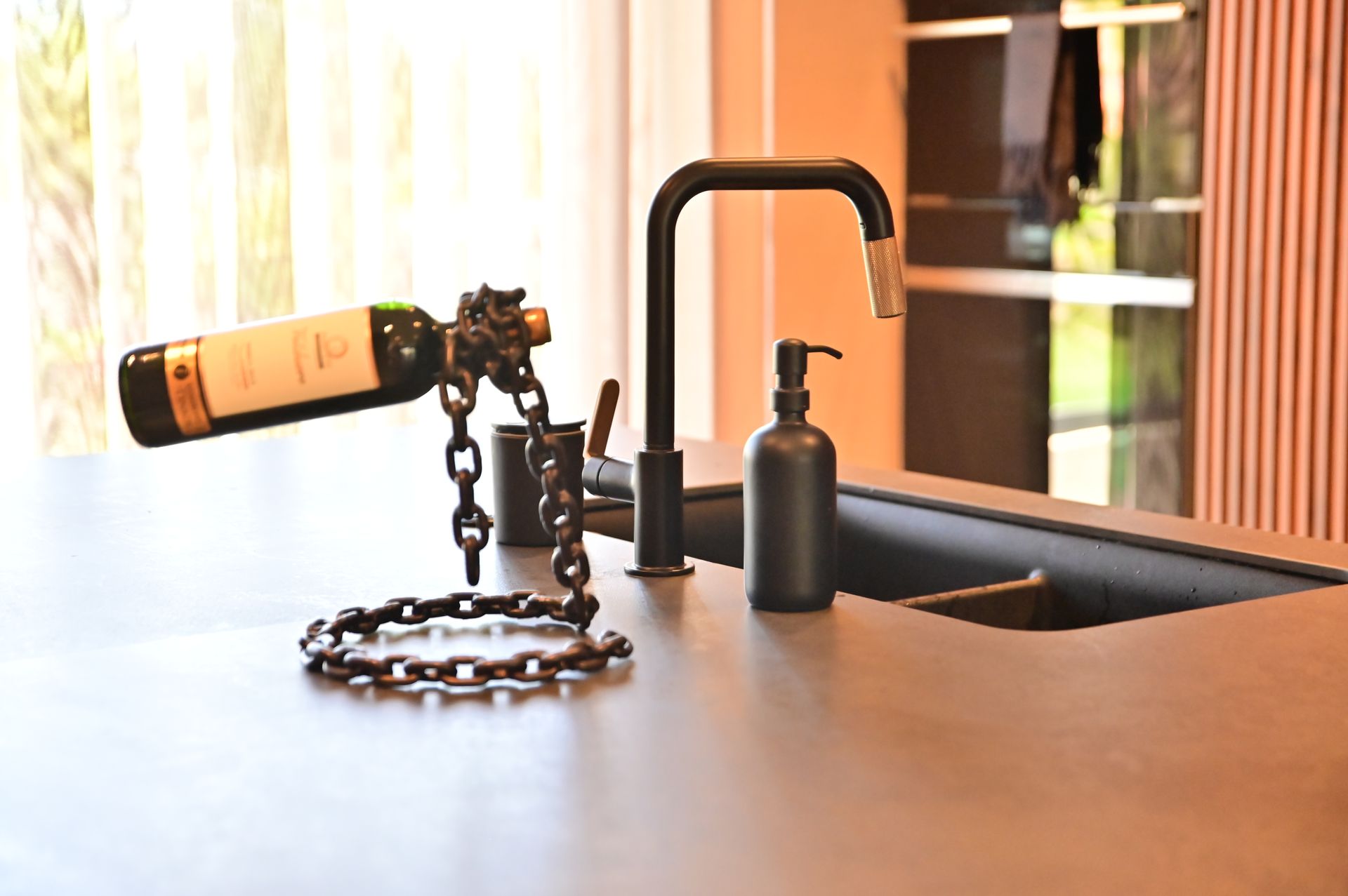 A kitchen counter with a wine bottle held by a chain, black faucet, and soap dispenser designed and built by DEV Builders Group