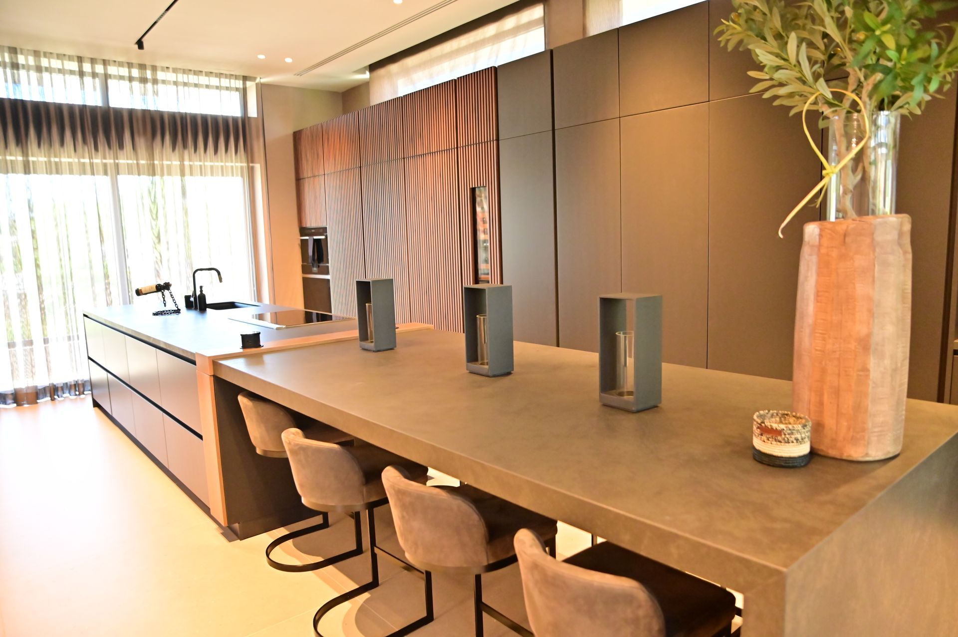 A kitchen with a long luxury counter and chairs and a vase of flowers on it designed and built by DEV Builders.