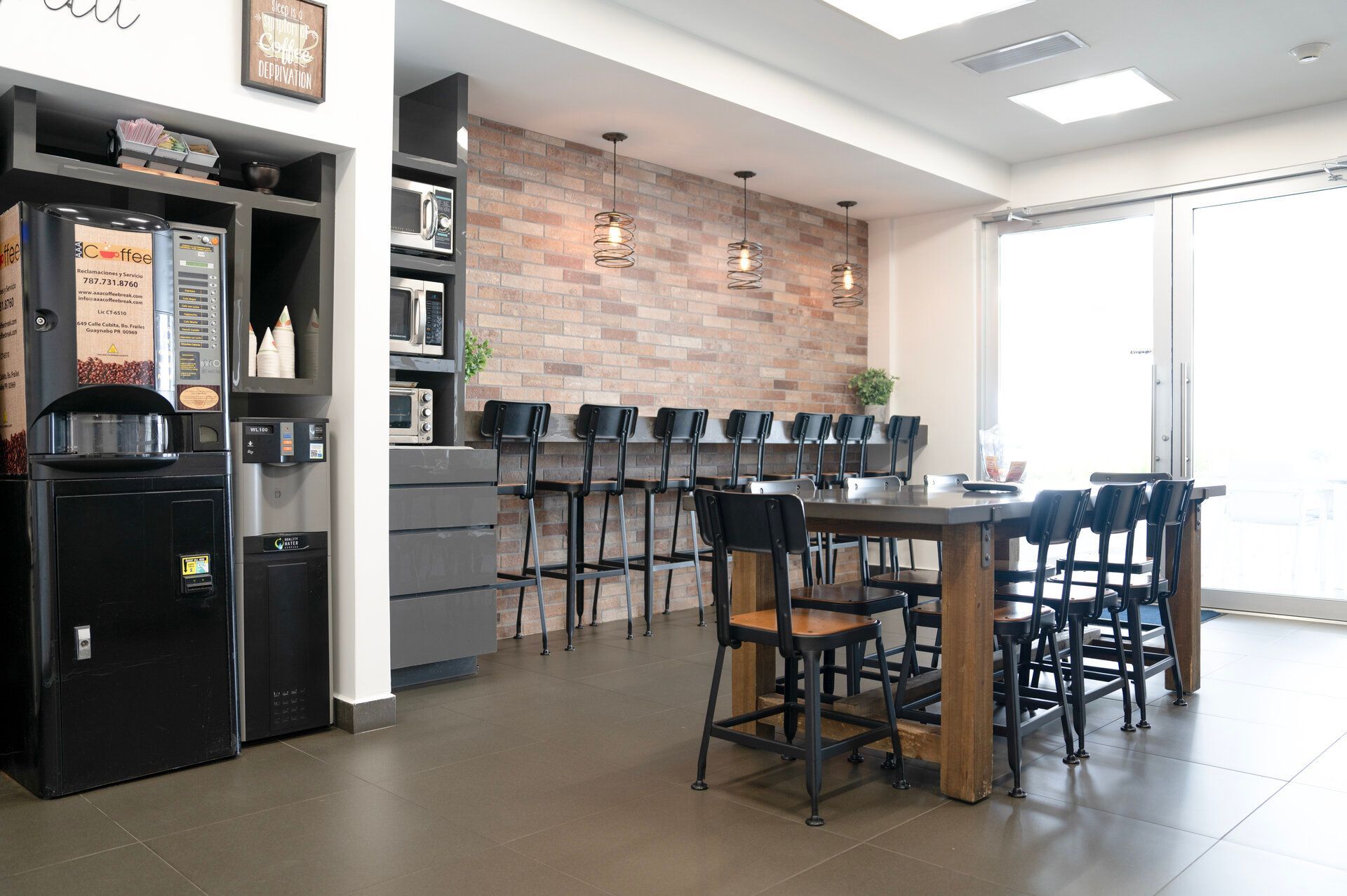 A break room with coffee machine, brick wall, tables, and chairs.