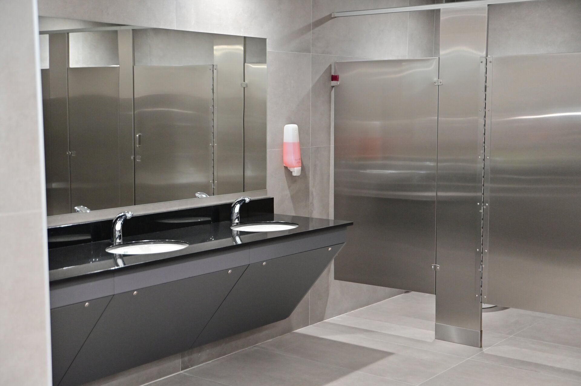 Modern restroom with stainless steel partitions, sinks, and a soap dispenser in Puerto Rico.