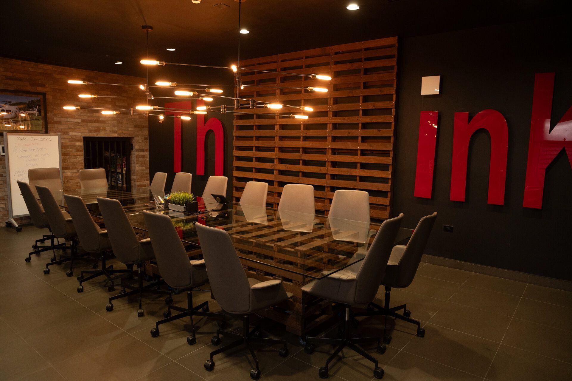 Conference room with large glass table, grey chairs, and wooden pallet wall,