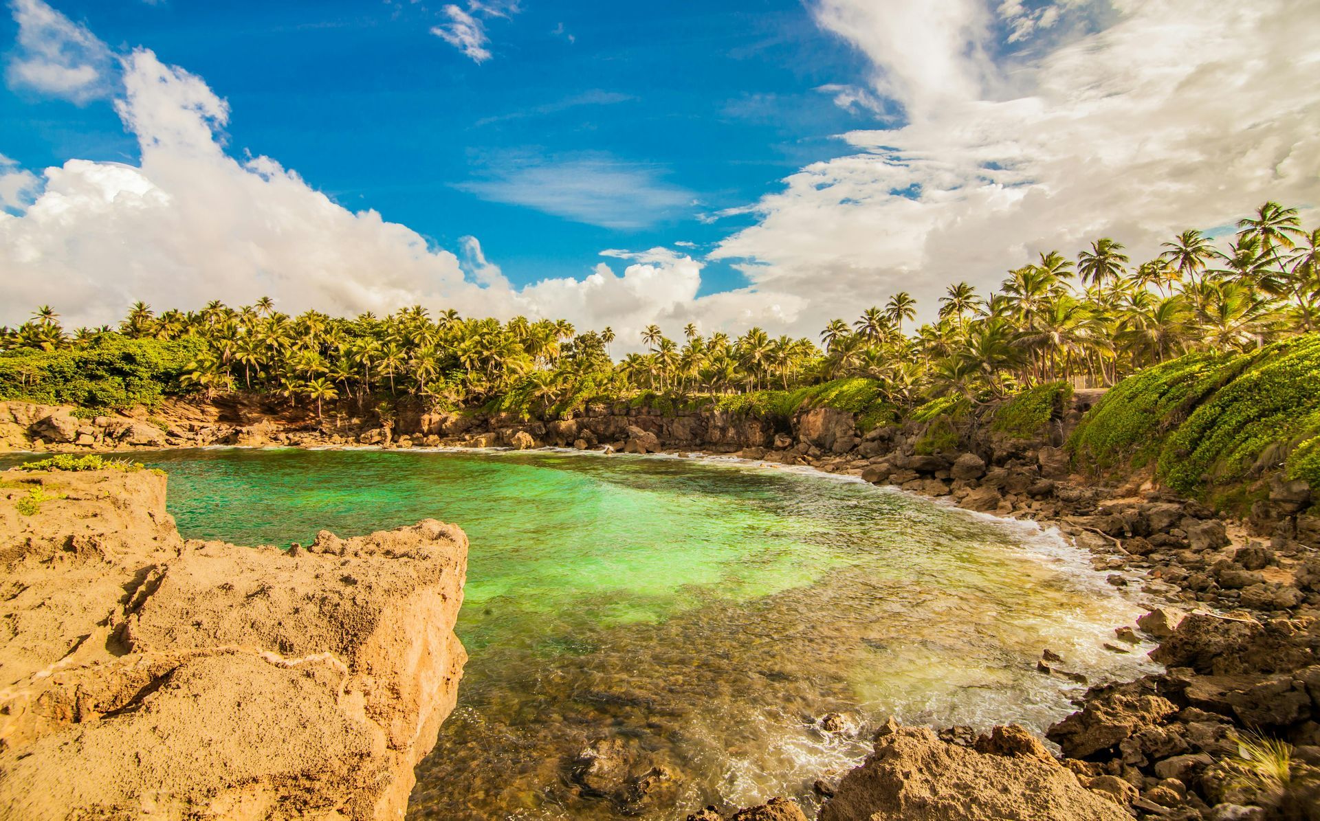 Bright lagoon with turquoise water surrounded by rocky cliffs and lush green trees under a blue sky with clouds.