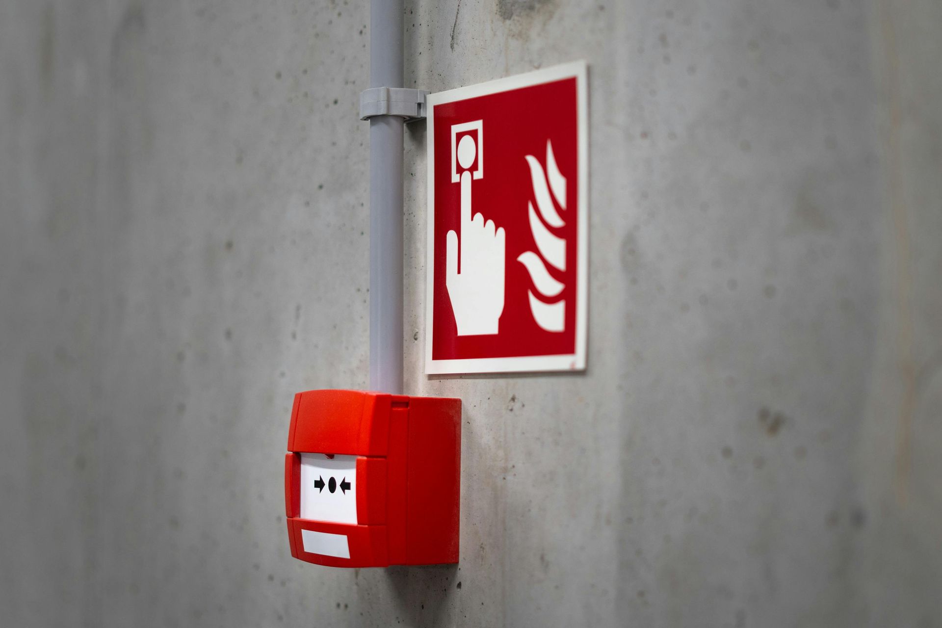 Red fire alarm button on a concrete wall with a sign showing a hand pressing a button and flames designed by DEV Builders.