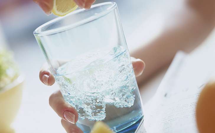 A person is squeezing a lemon into a glass of water.