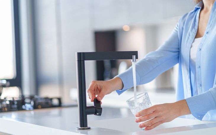 A woman is pouring water from a faucet into a glass.