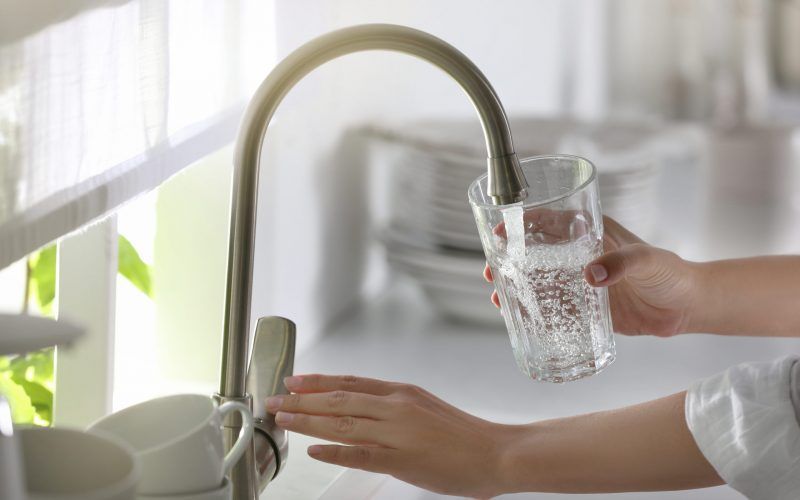 A person is pouring water into a glass from a faucet.