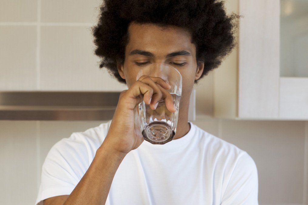 A man is drinking a glass of water in a kitchen.