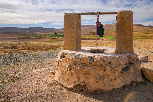 A stone well in the middle of a desert with a bucket hanging from it.