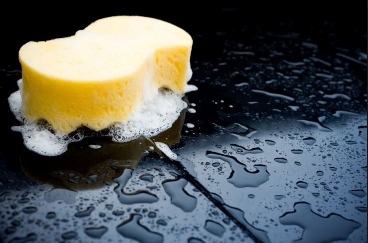 A yellow sponge is sitting on a black surface with water drops