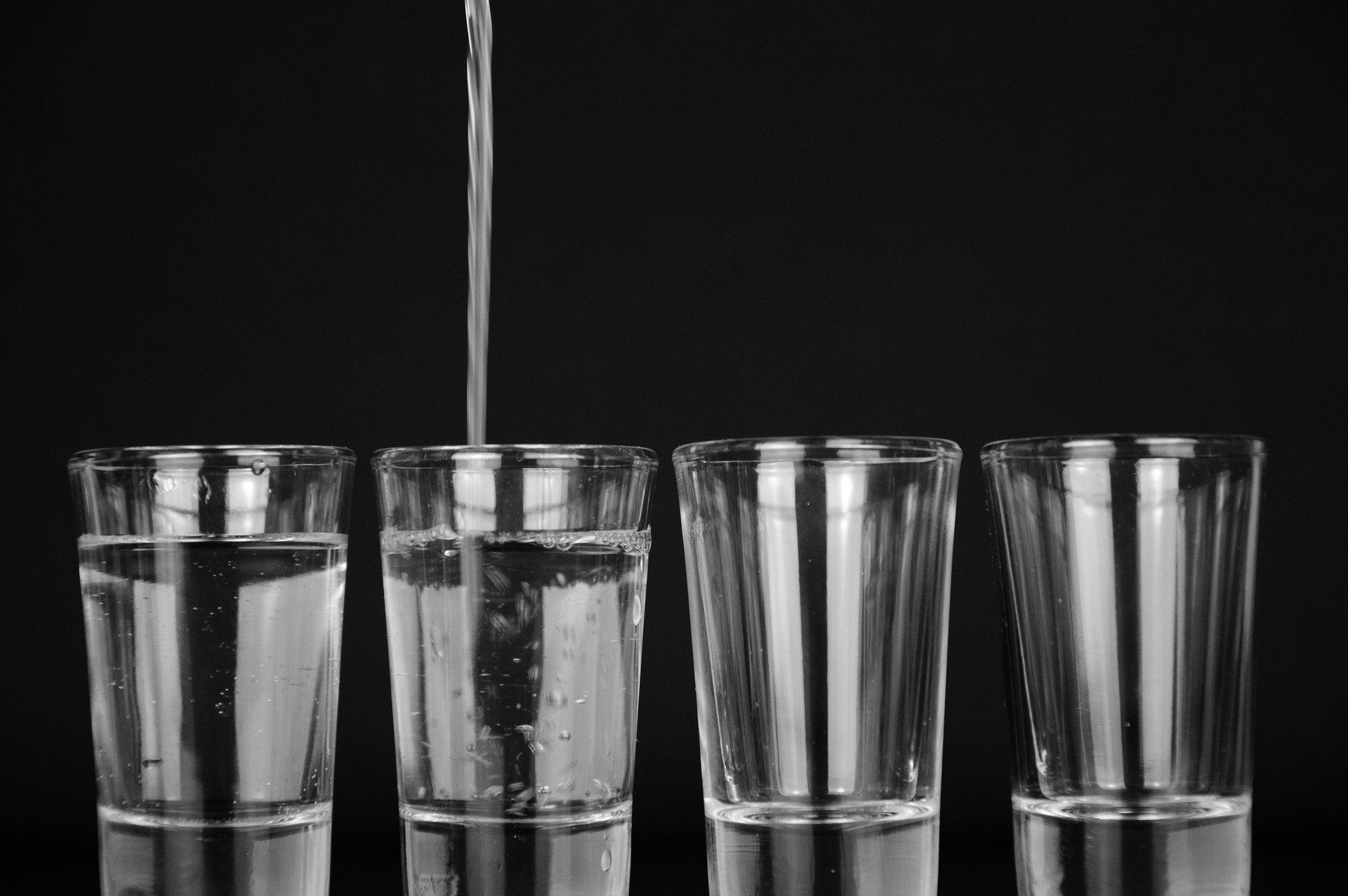 Water is being poured into four glasses on a black background.