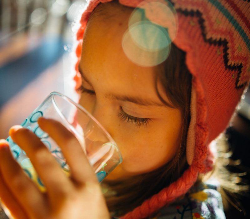 A little girl wearing a pink hat is drinking from a glass.