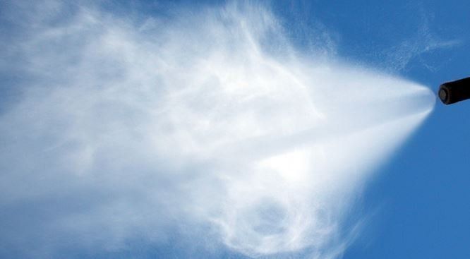 A person is spraying water from a hose against a blue sky.