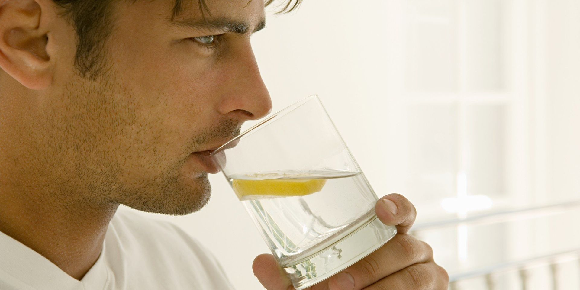 A man is drinking a glass of water with a lemon slice in it.