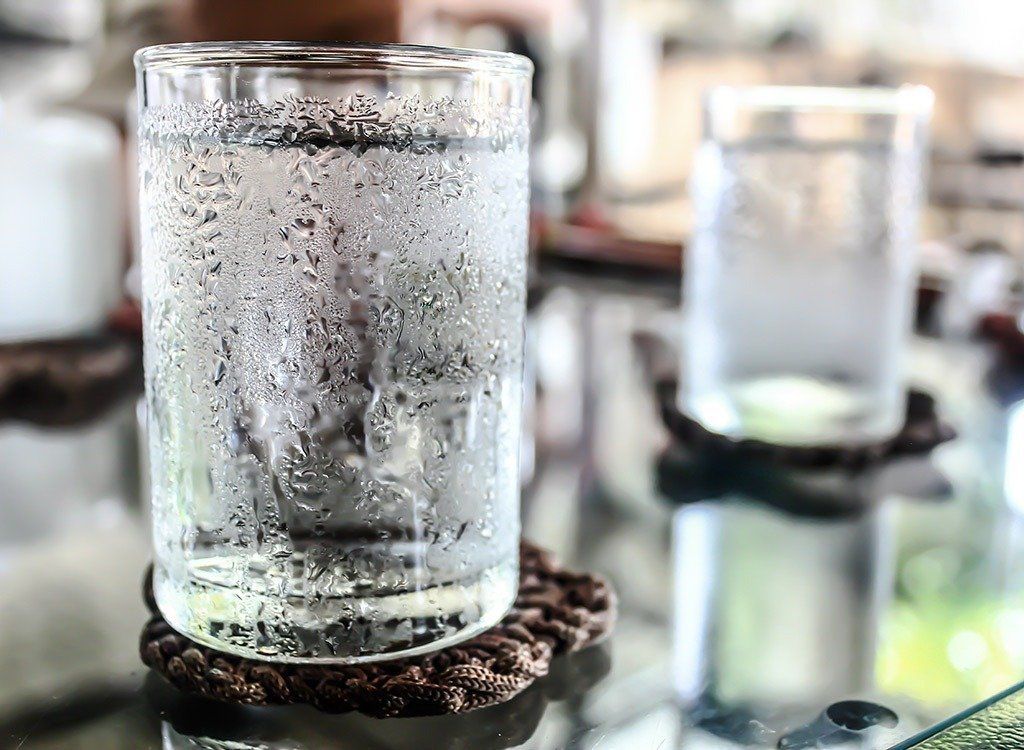 A glass of water is sitting on a wooden coaster on a table.