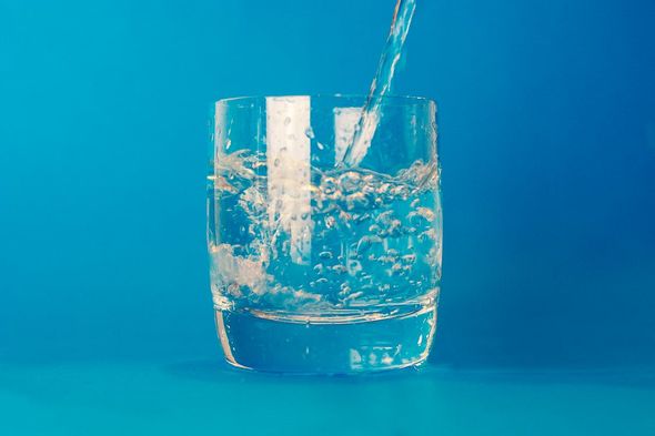 Water is being poured into a glass on a blue background.