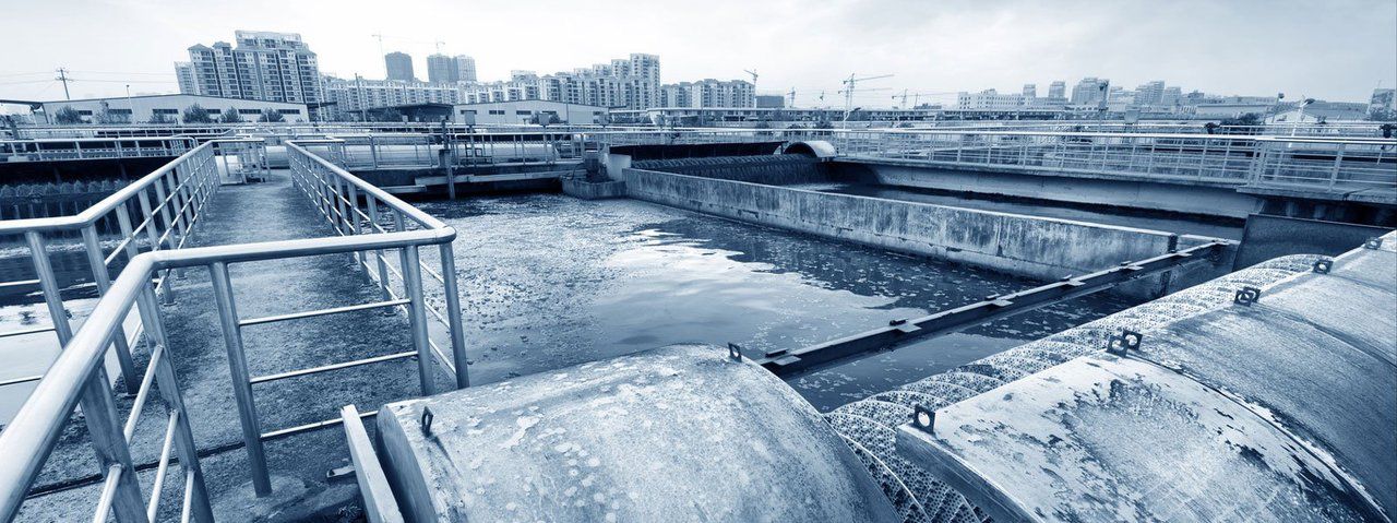 A black and white photo of a water treatment plant with a city in the background.