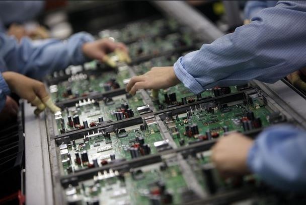 A group of people are working on a motherboard in a factory.