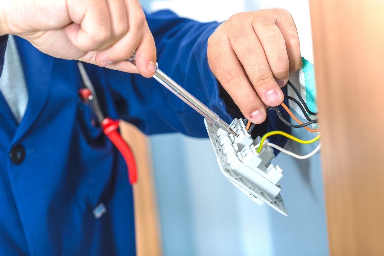 Electrician installing an electrical outlet, holding a screwdriver, in a blue work suit.