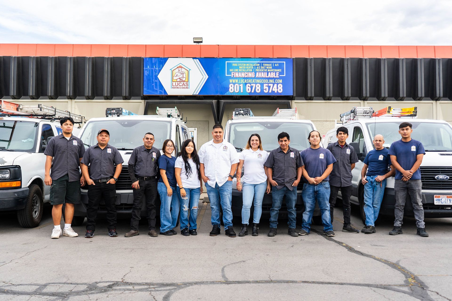 Group of people in front of company trucks; building background.
