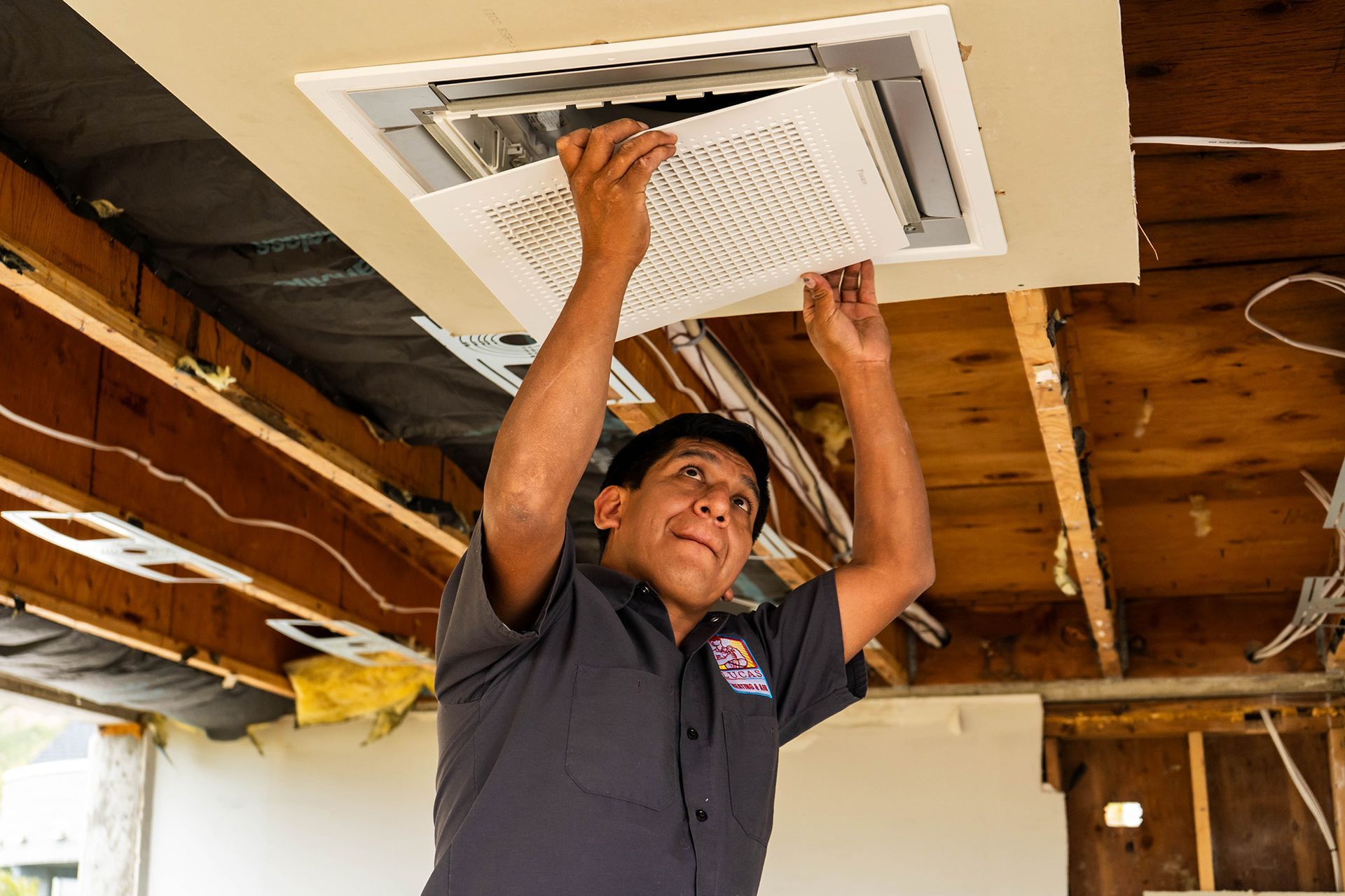 Man in uniform installing ceiling air conditioning unit.