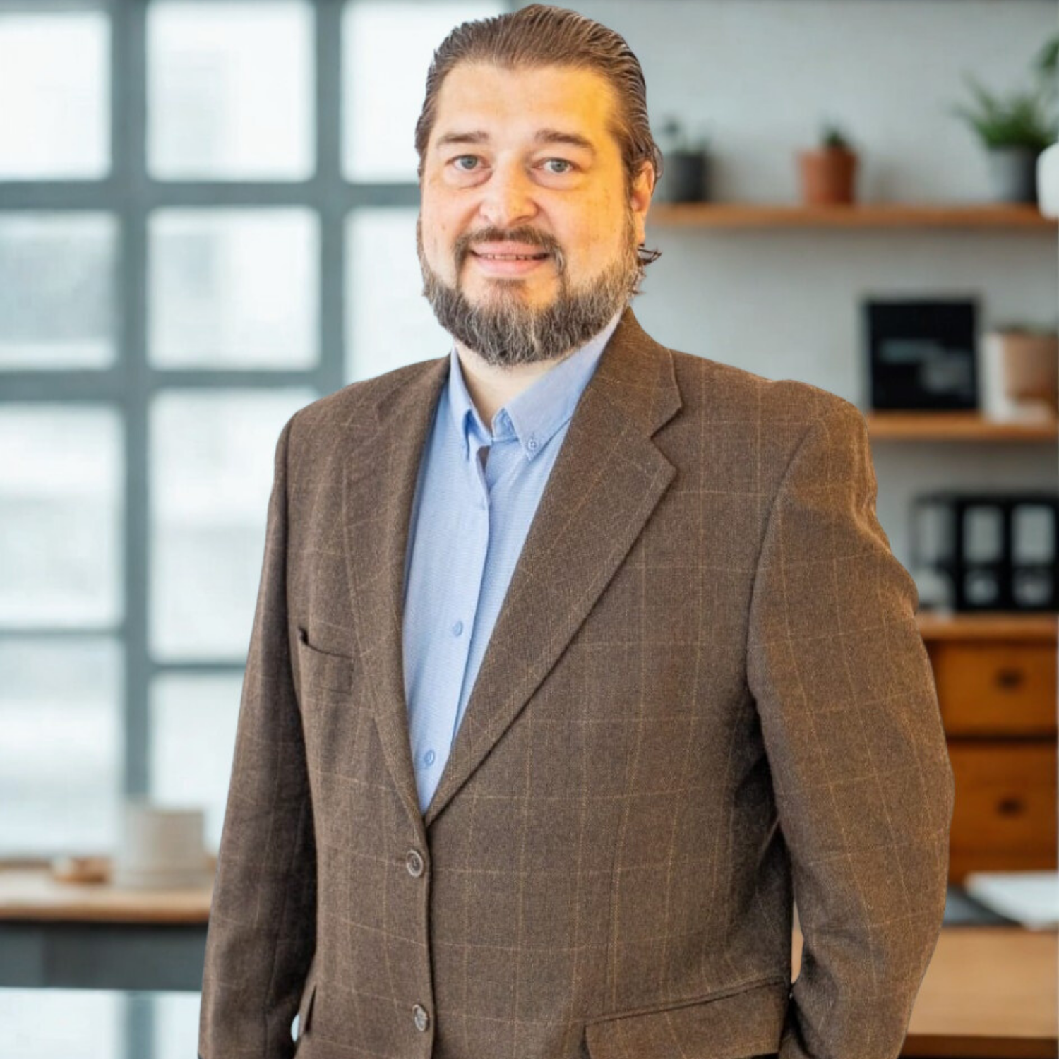 Um homem com barba vestindo uma jaqueta marrom e uma camisa azul