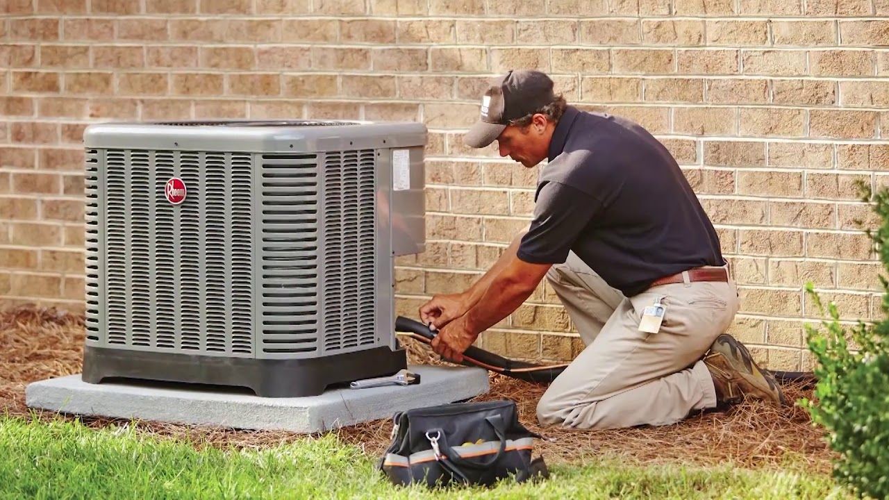 A man is working on an air conditioner outside of a brick building.
