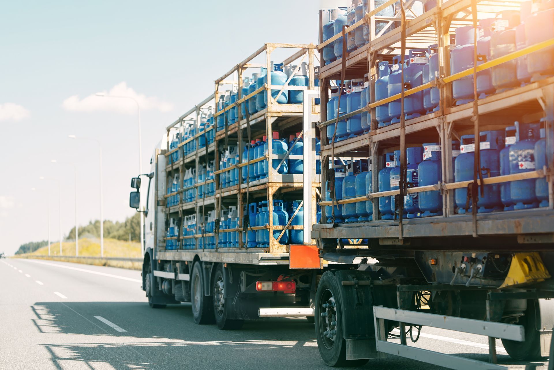 Truck transporting rows of blue gas cylinders secured on racks along a highway.
