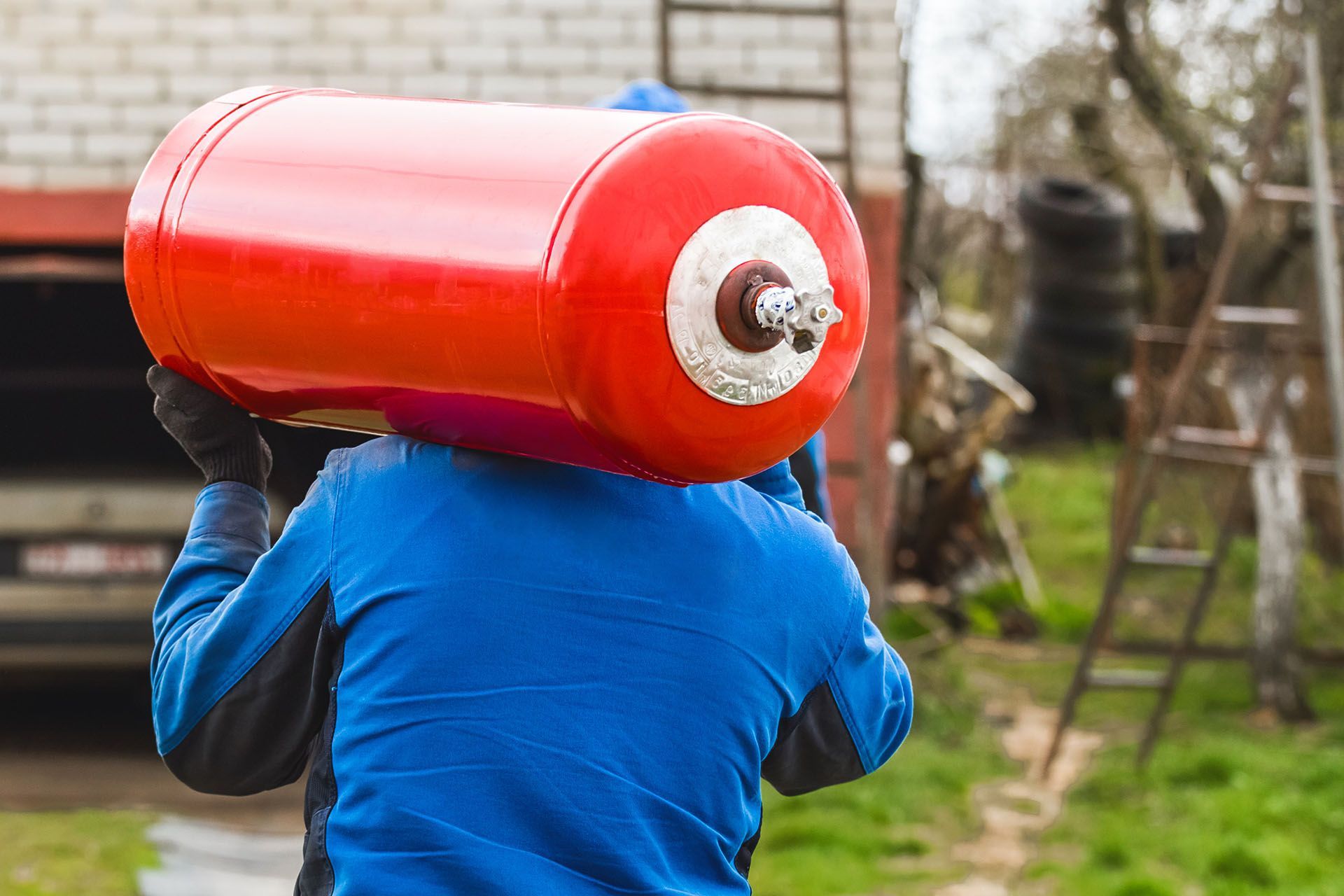 A man is carrying a gas tank on his shoulder.