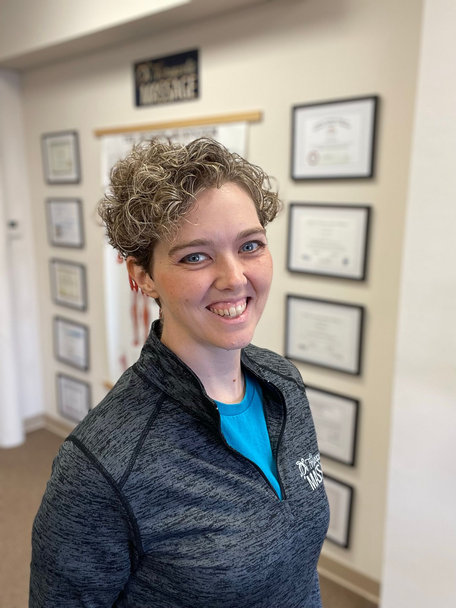 A woman is smiling in front of a wall with certificates on it.