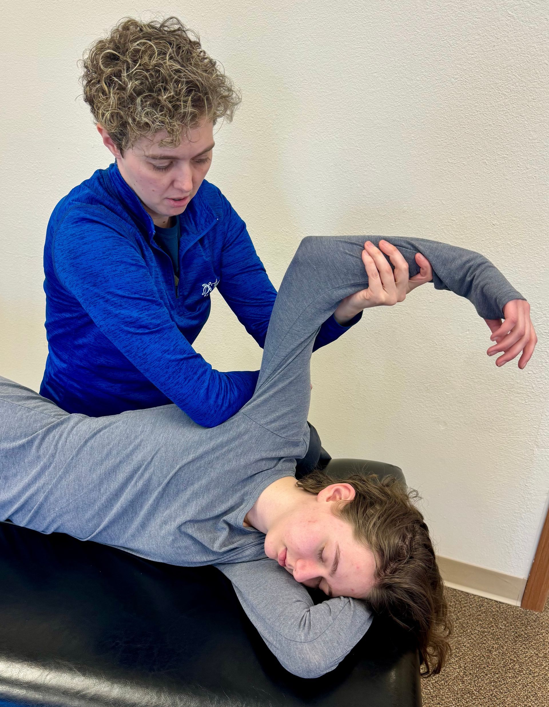 A woman is stretching a man 's arm on a table.