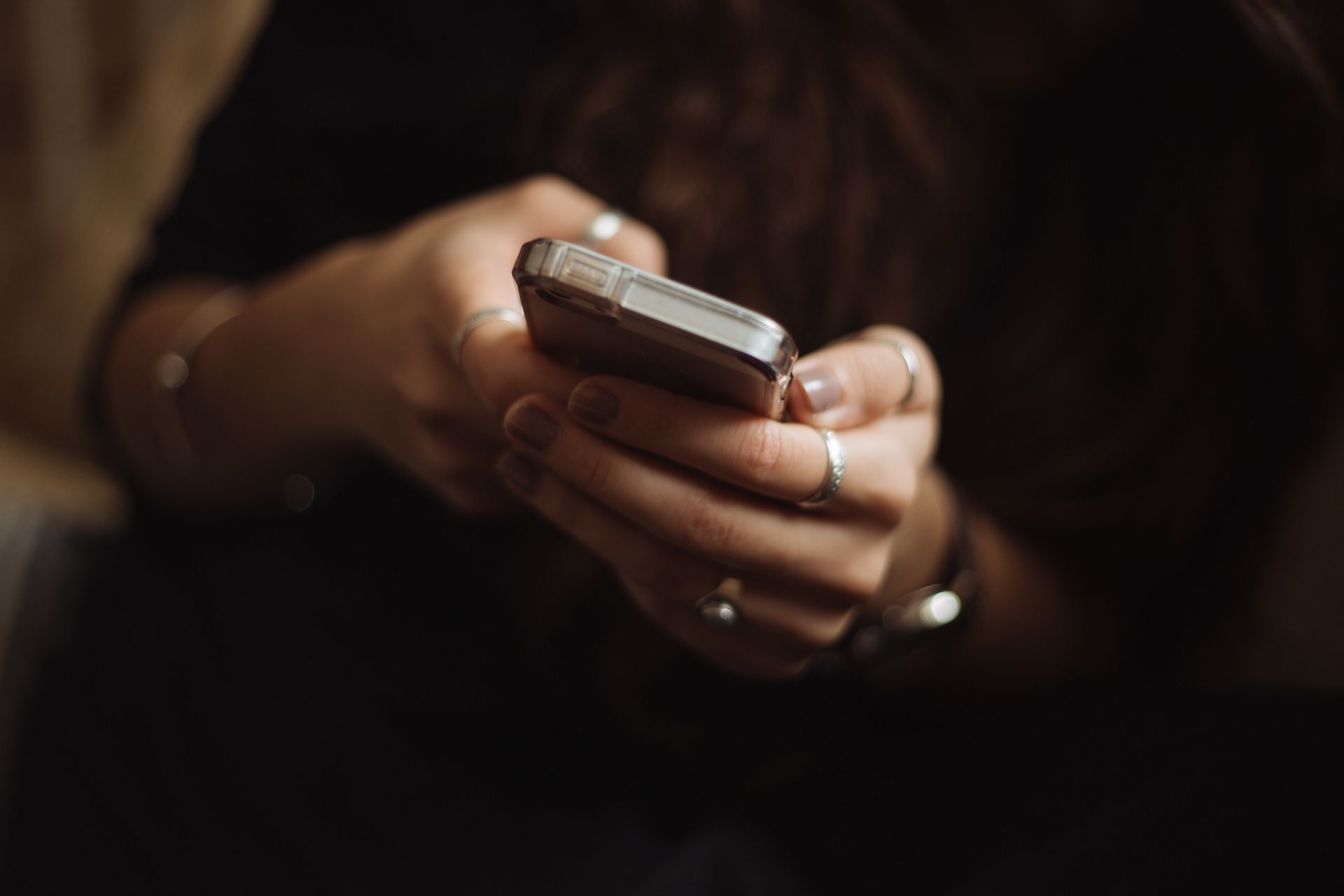 Woman's hands holding a smartphone, typing. Rings and bracelets are visible.