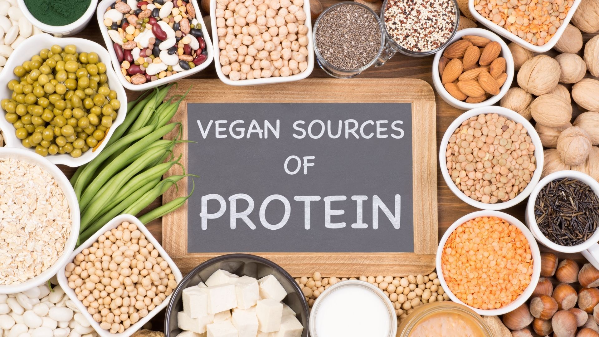 A variety of vegan sources of protein are displayed on a wooden table.