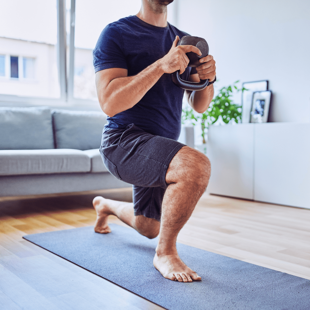 A man is squatting on a yoga mat while holding a kettlebell.