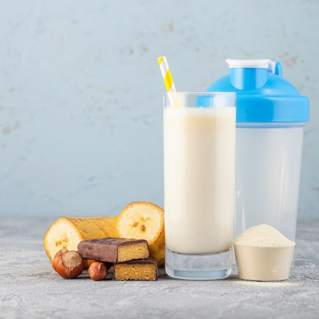 A glass of milk with a straw , a shaker , and bananas on a table.