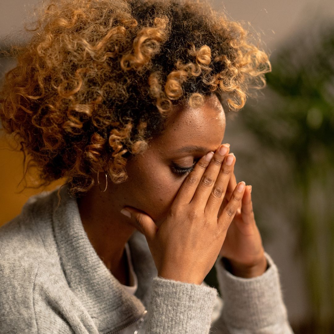 A woman with curly hair is covering her face with her hands.