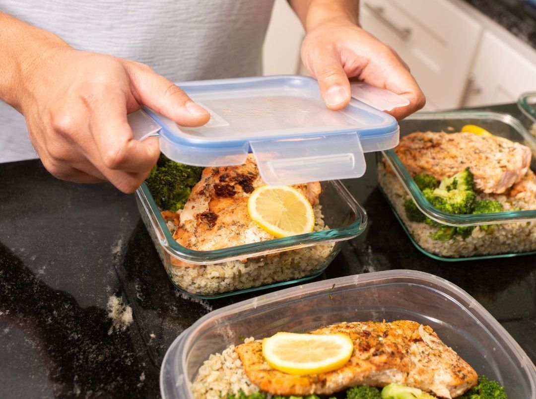 A man is putting food in a plastic container on a counter.