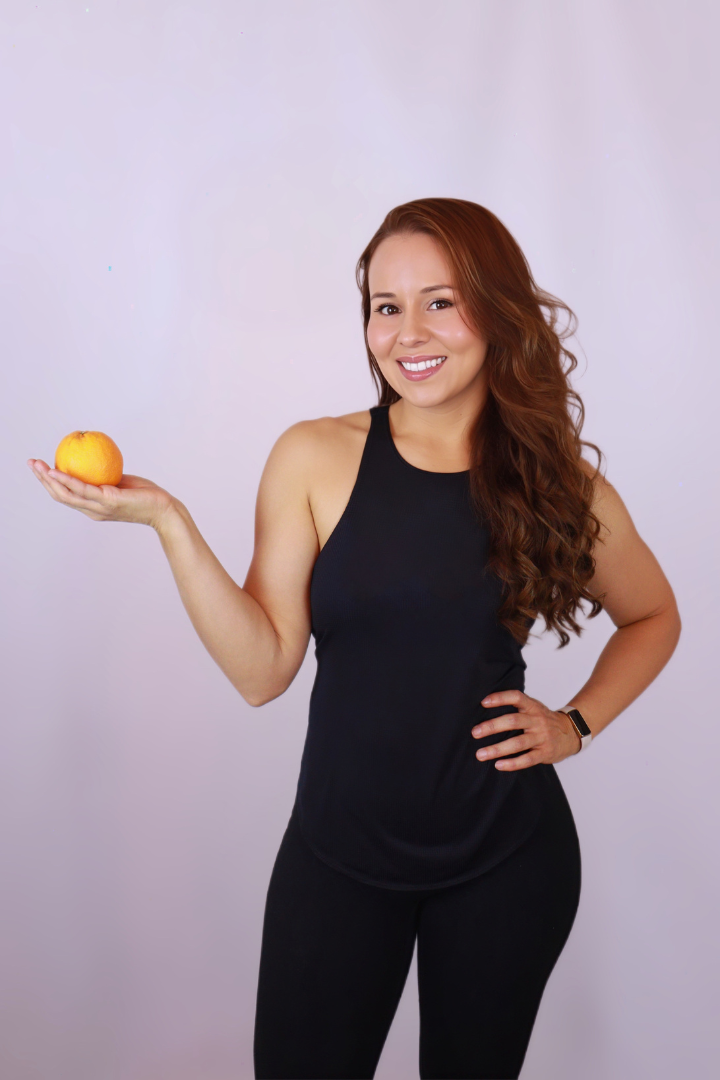 A woman in a black tank top is holding an orange in her hand