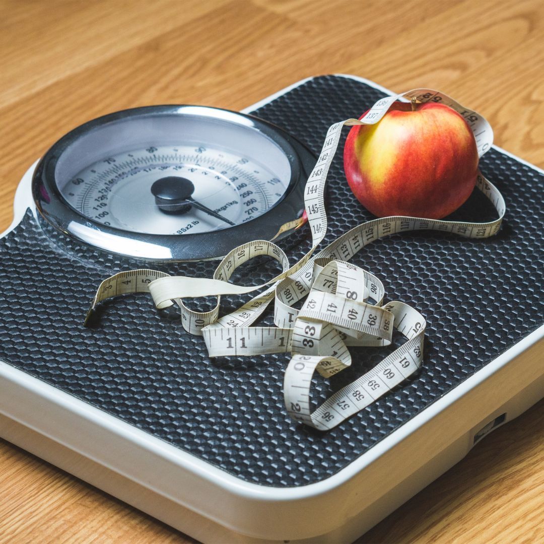 A scale with an apple and measuring tape on it