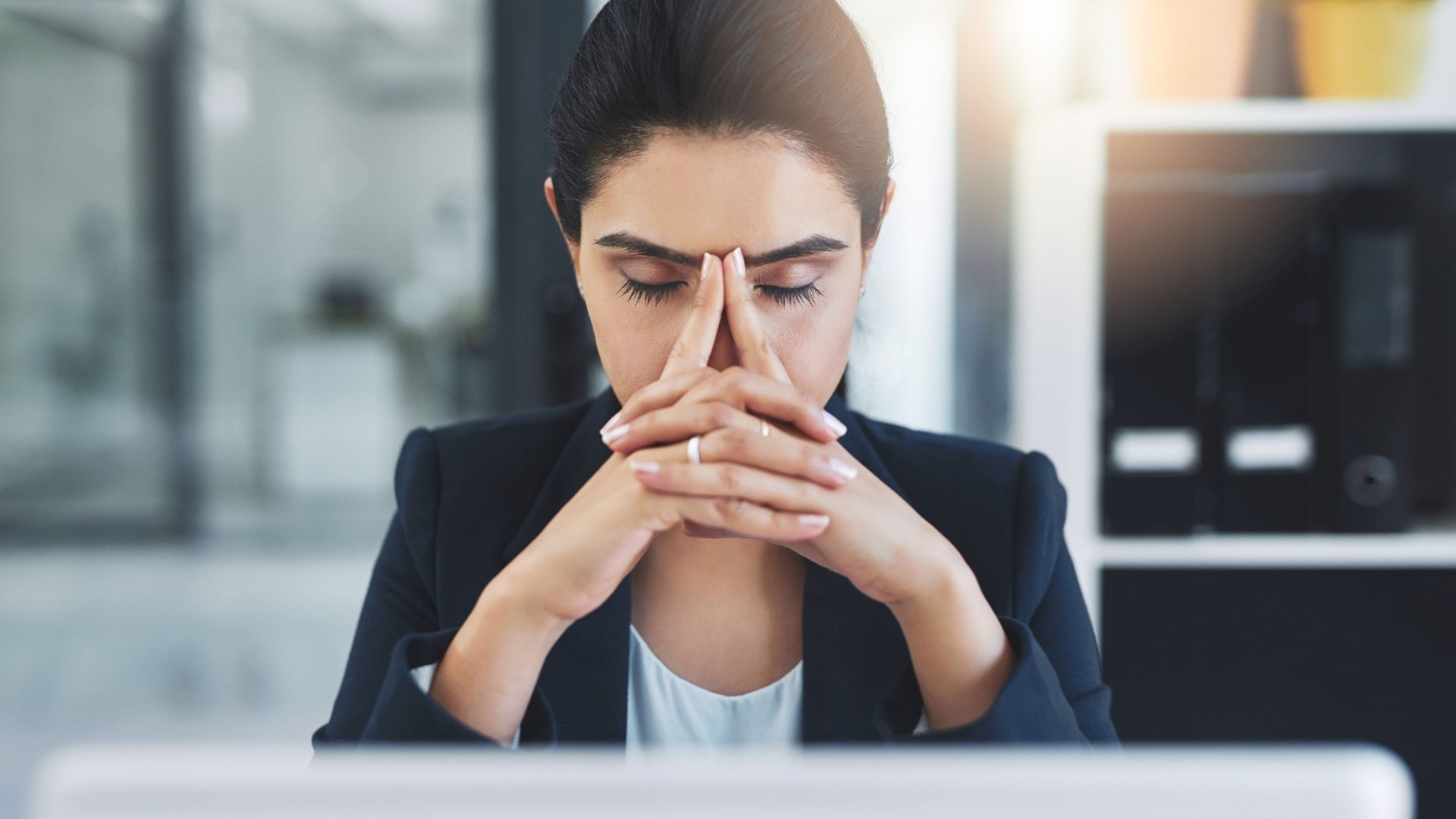 A woman is sitting in front of a laptop computer with her hands on her face.