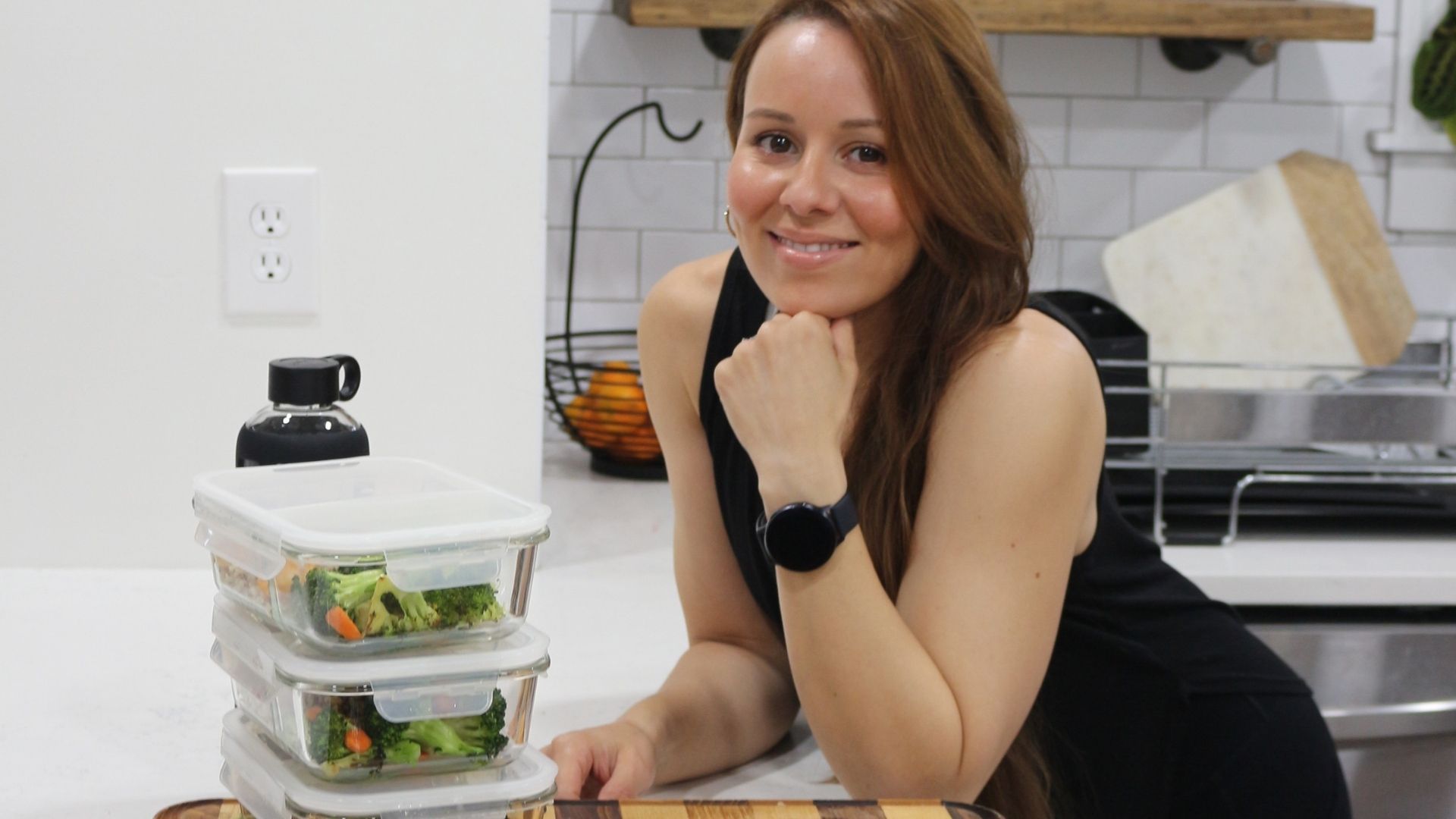 A woman is sitting at a counter in a kitchen with containers of food.