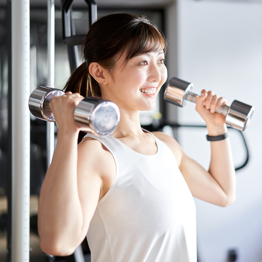 A woman is lifting dumbbells in a gym and smiling. Strength Training and Nutritional Coaching