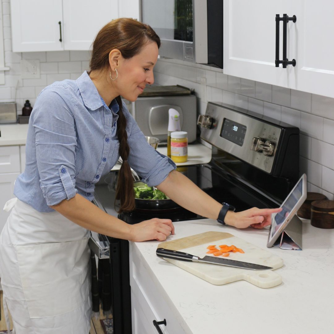 A woman is cooking in a kitchen and using a tablet