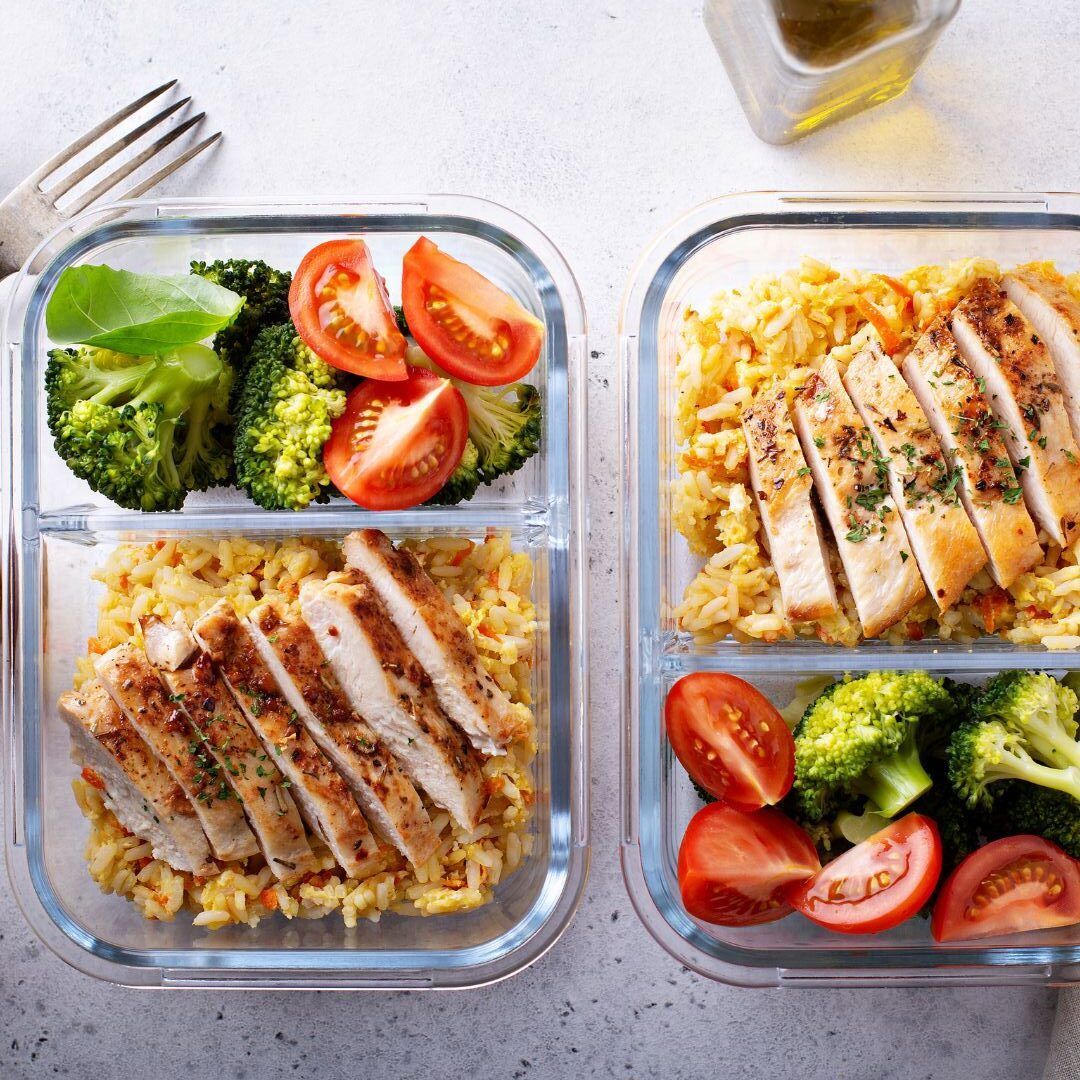 Two glass containers filled with chicken , broccoli , tomatoes and rice.